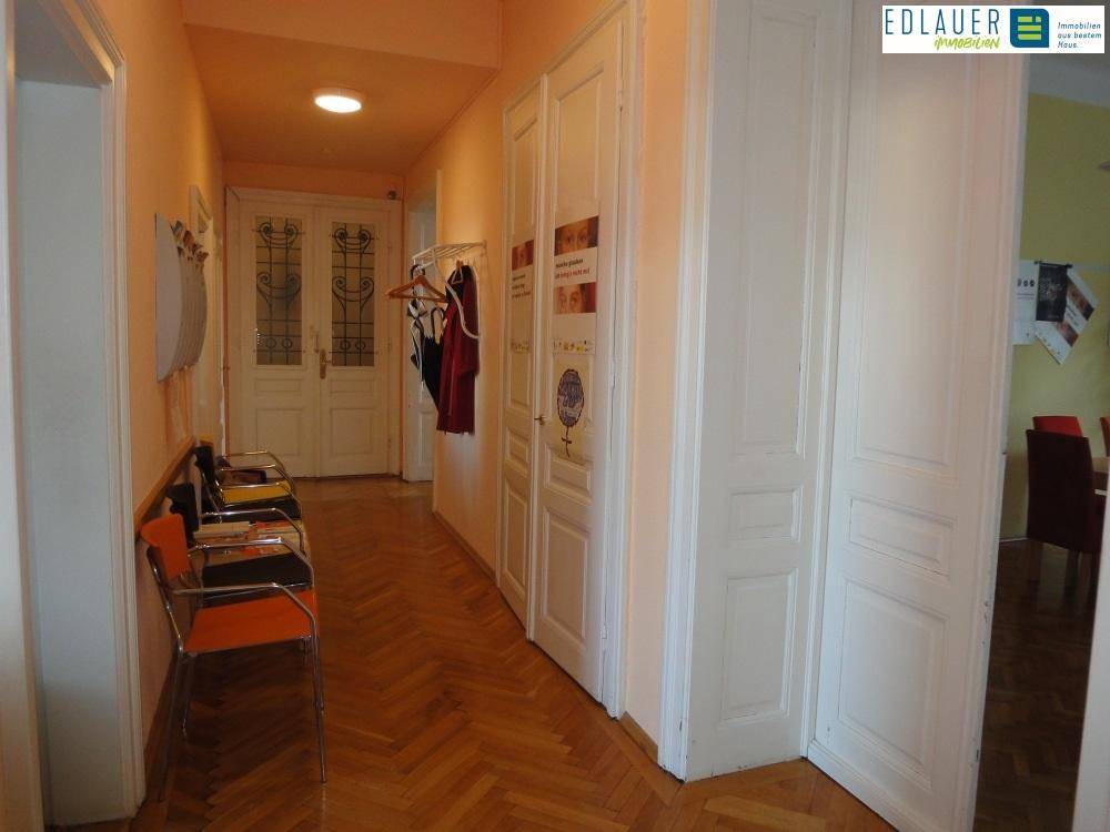 Langer Flur mit Fischgrätparkett, weißen Türen und einer Garderobe, der zu weiteren Räumen führt.