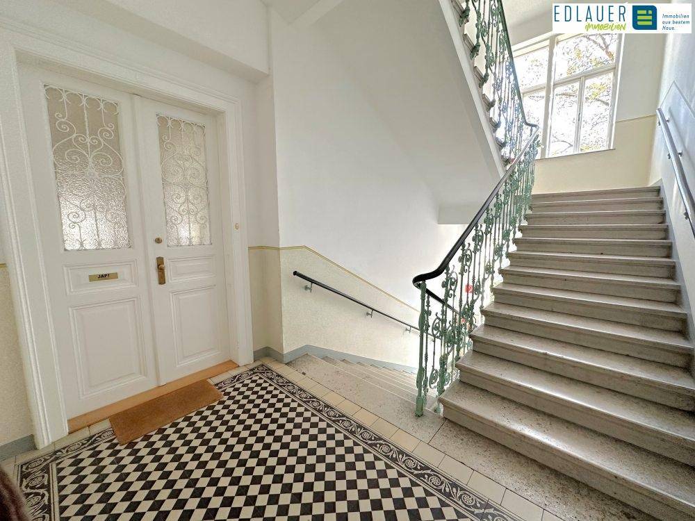 Historisches Treppenhaus mit Marmorstufen, schmiedeeisernem Geländer und großen Fenstern, die viel Licht hereinlassen.