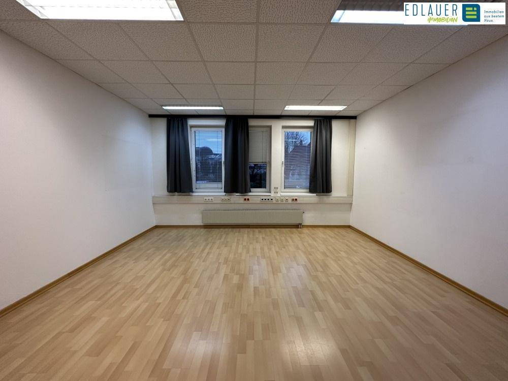 Leerer Büroraum mit Laminatboden, weißen Wänden und zwei Fenstern, ideal für flexible Nutzung.