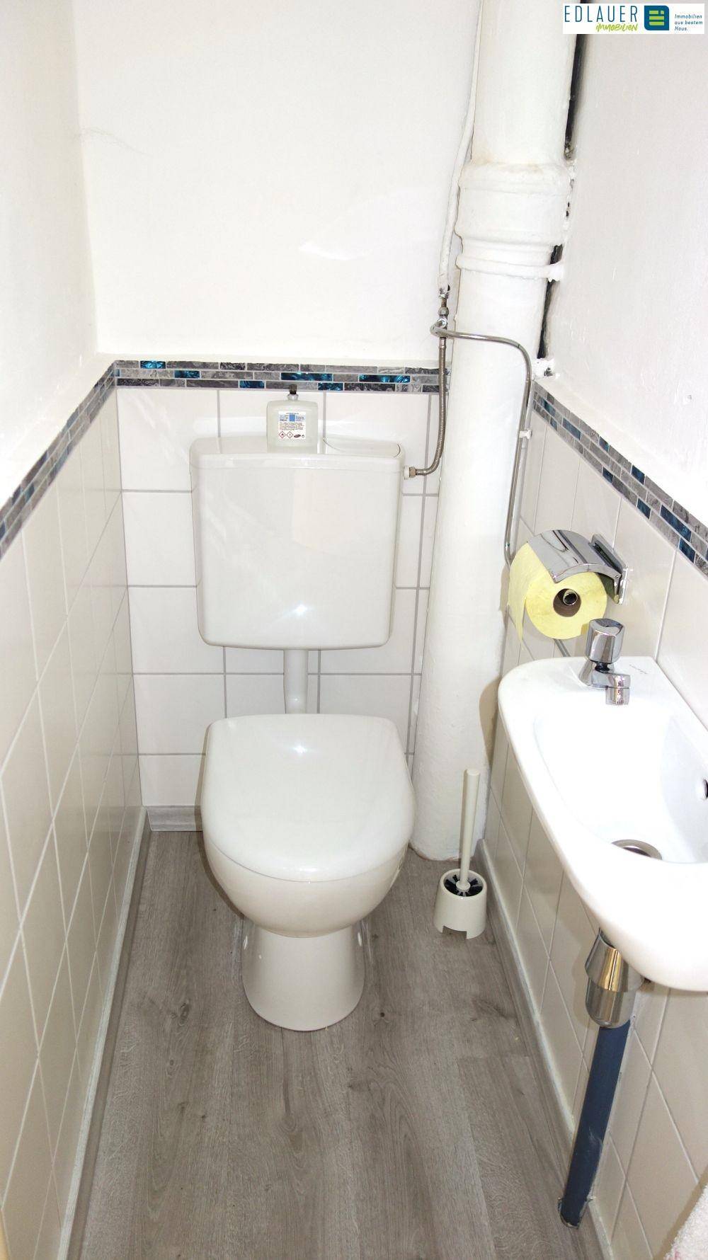 Kleines WC mit Toilette, Waschbecken und weißen Fliesen, sauber und funktional.