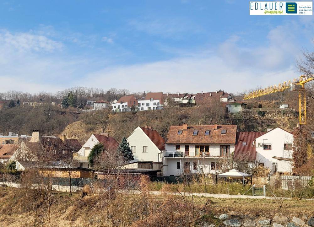 Panoramablick auf eine Wohnsiedlung am Hang mit verschiedenen Häusern und einem Baukran im Hintergrund.