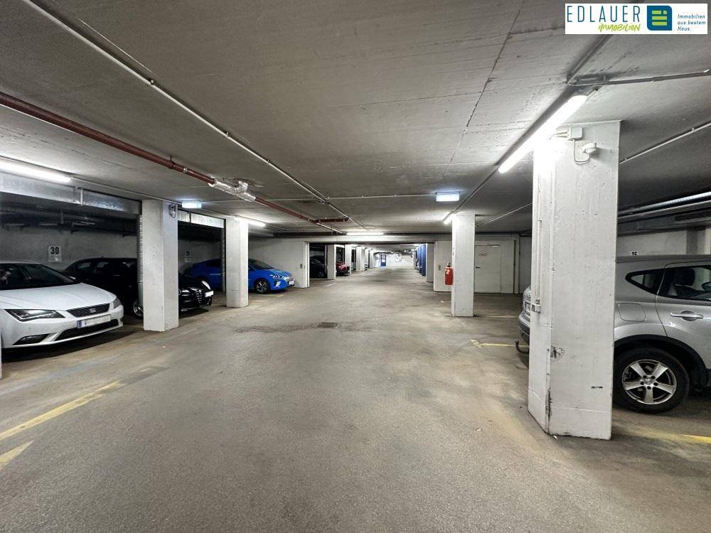 Geräumige Tiefgarage mit markierten Parkplätzen und abgestellten Fahrzeugen entlang der Säulen.