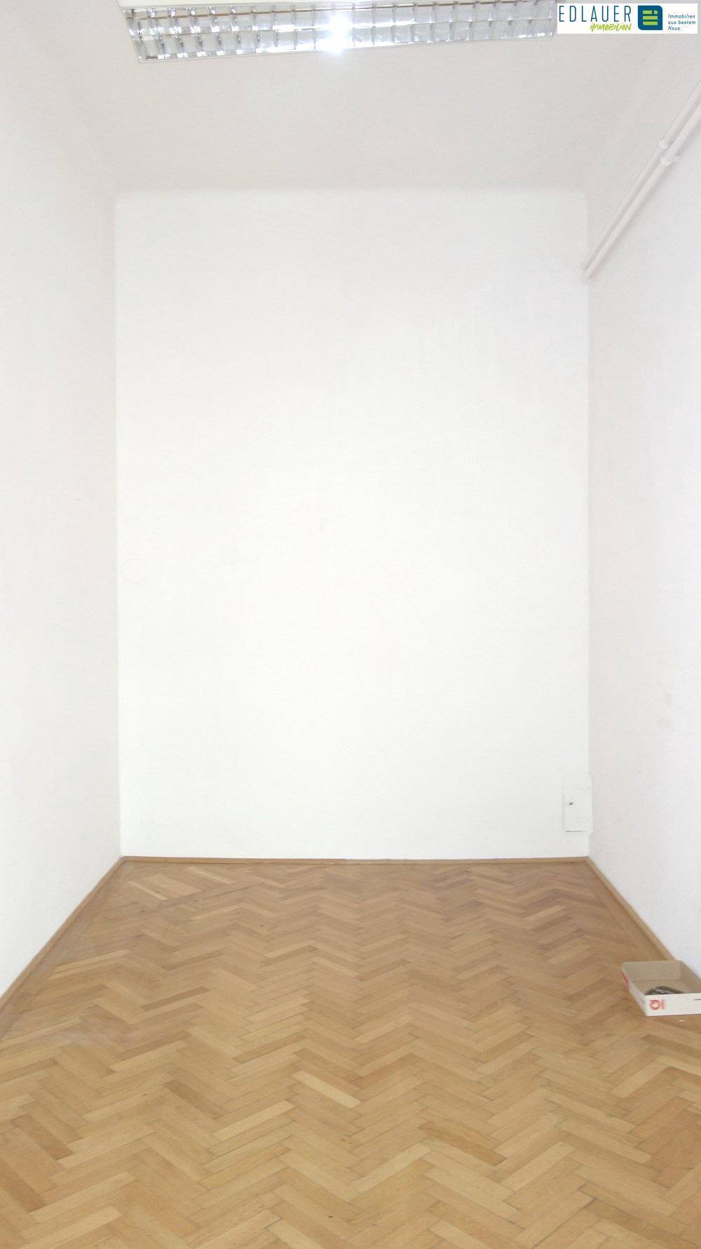 Schlichter, leerer Raum mit Fischgrätparkett und Deckenleuchten, geeignet für verschiedene gewerbliche Nutzungen.