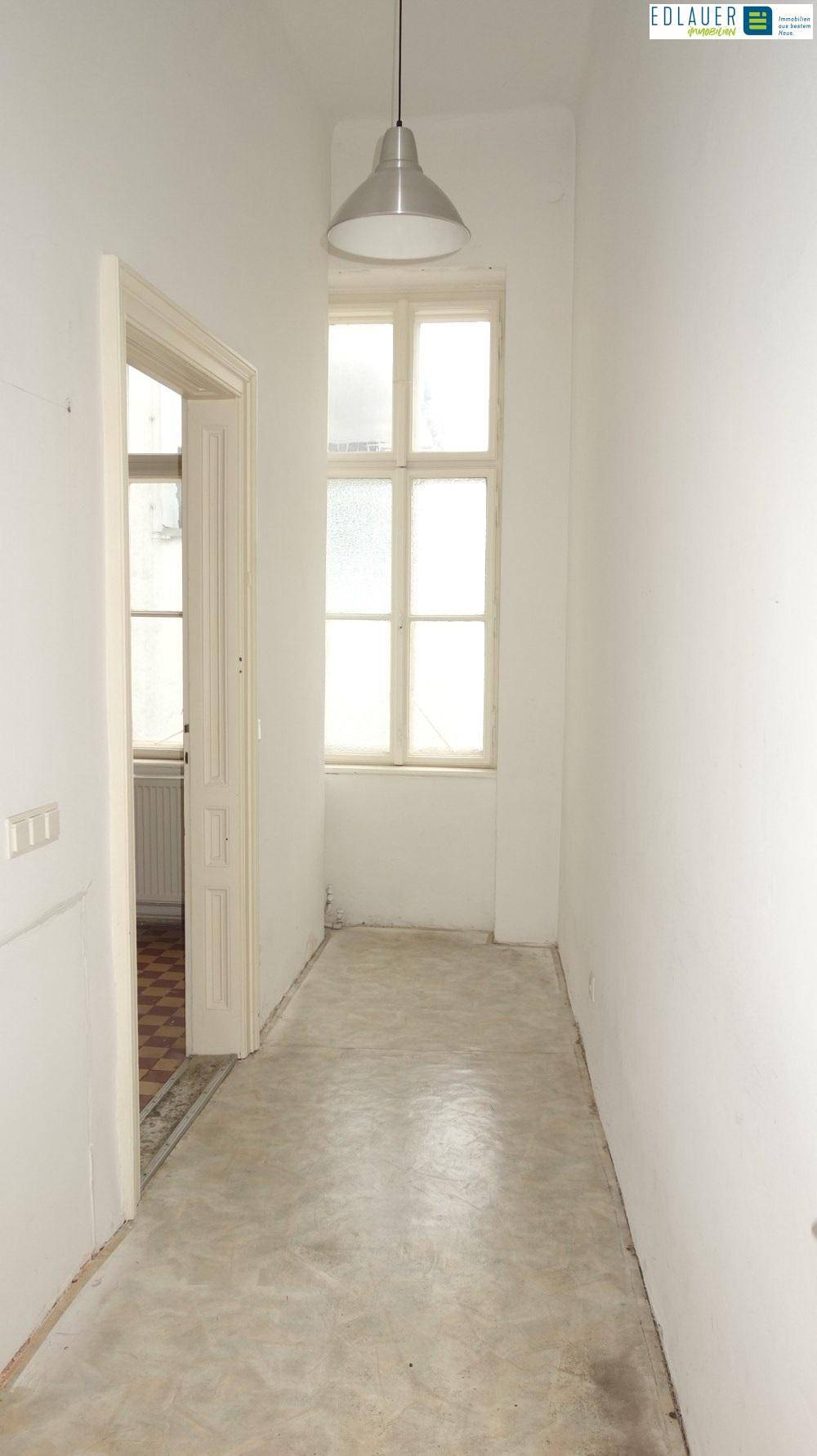 Langer Flur mit Betonboden, einem Fenster und einer Pendelleuchte, der zu weiteren Räumen führt.