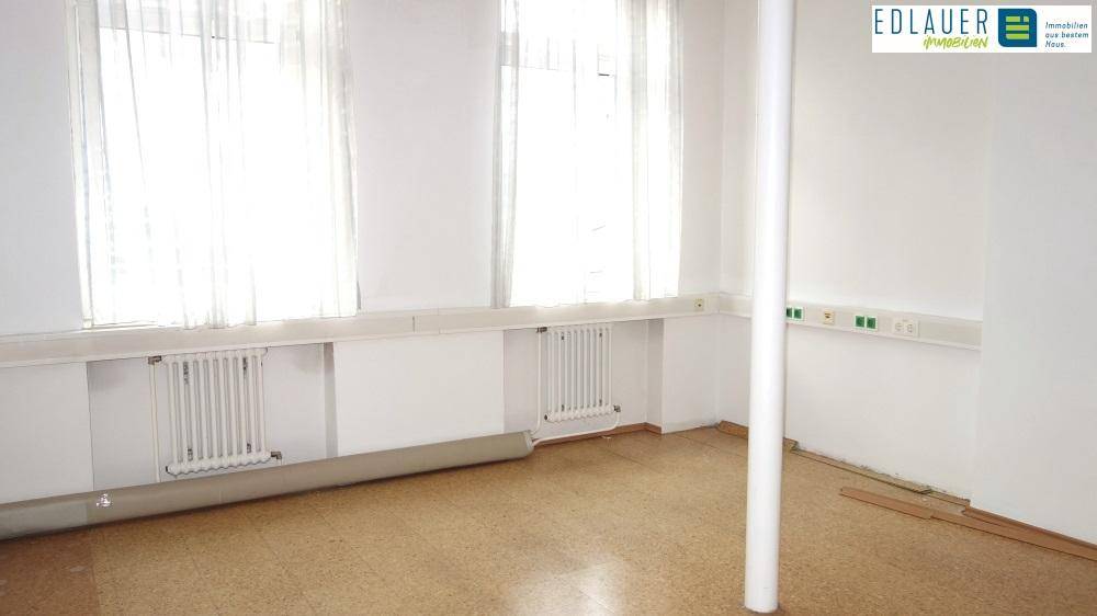 Leerer Büroraum mit großen Fenstern, Heizkörpern und Linoleumboden, bietet viel natürliches Licht.
