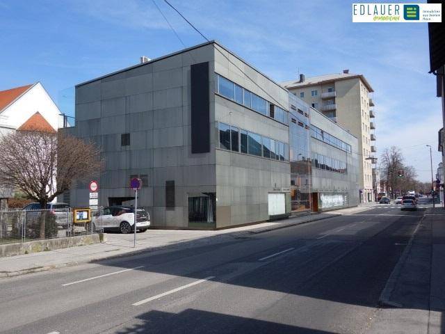 Ansicht des modernen Geschäftsgebäudes von der Straßenseite mit umliegenden Gebäuden und blauem Himmel.