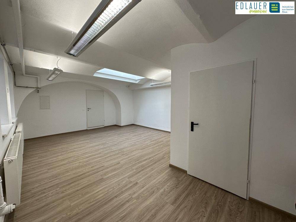 Geräumiger Raum mit Laminatboden, Tür und Heizkörper unter einem Fenster, gut beleuchtet durch Oberlicht.