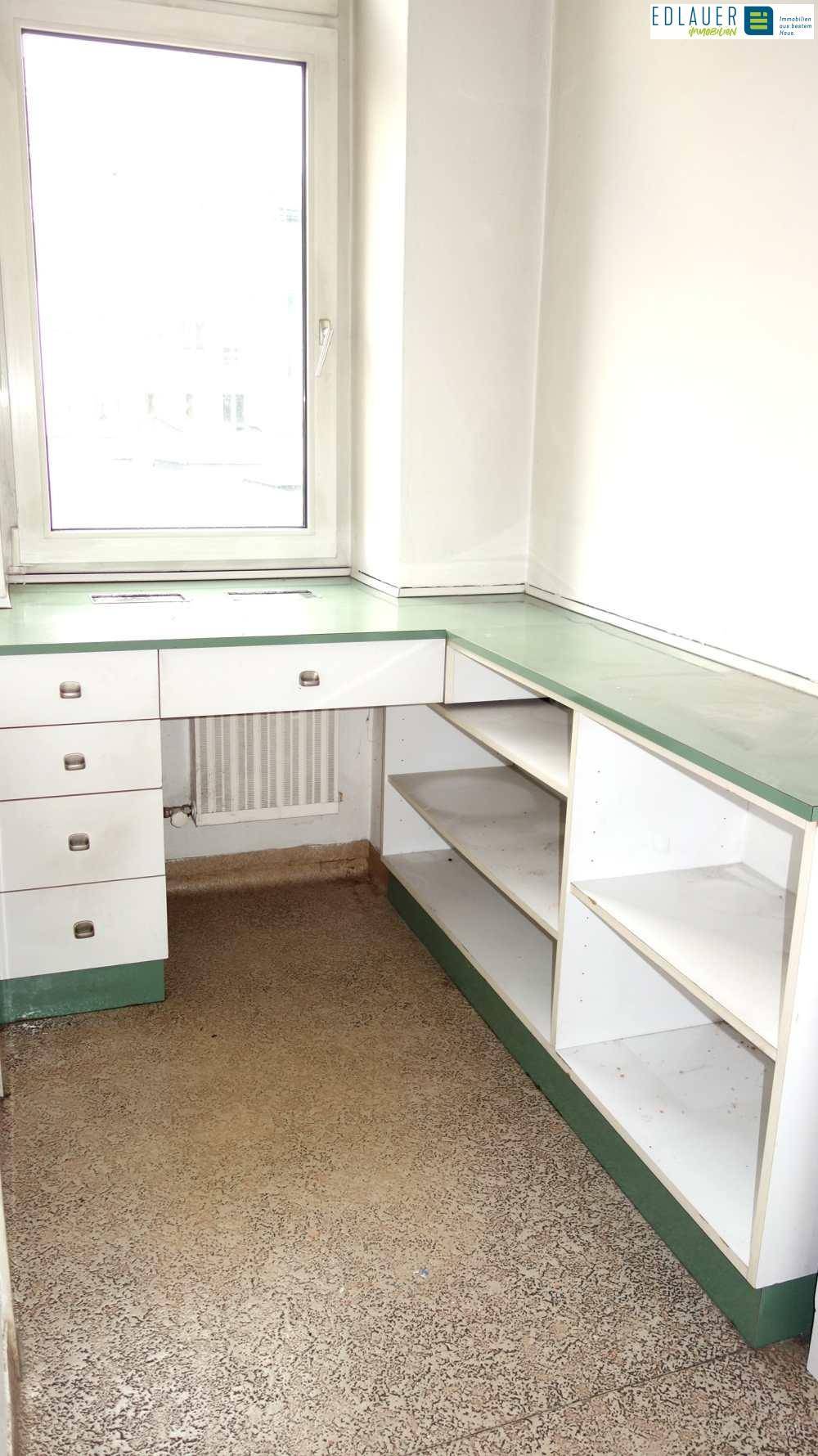 Kleiner Büroraum mit eingebautem Schreibtisch, Regalen und einem Fenster.