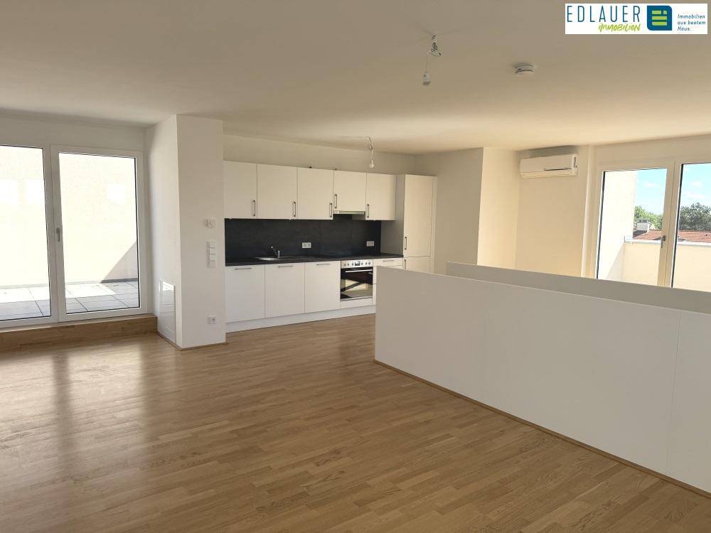 Heller offener Wohnbereich mit integrierter Küche, Parkettboden und Zugang zur Terrasse.