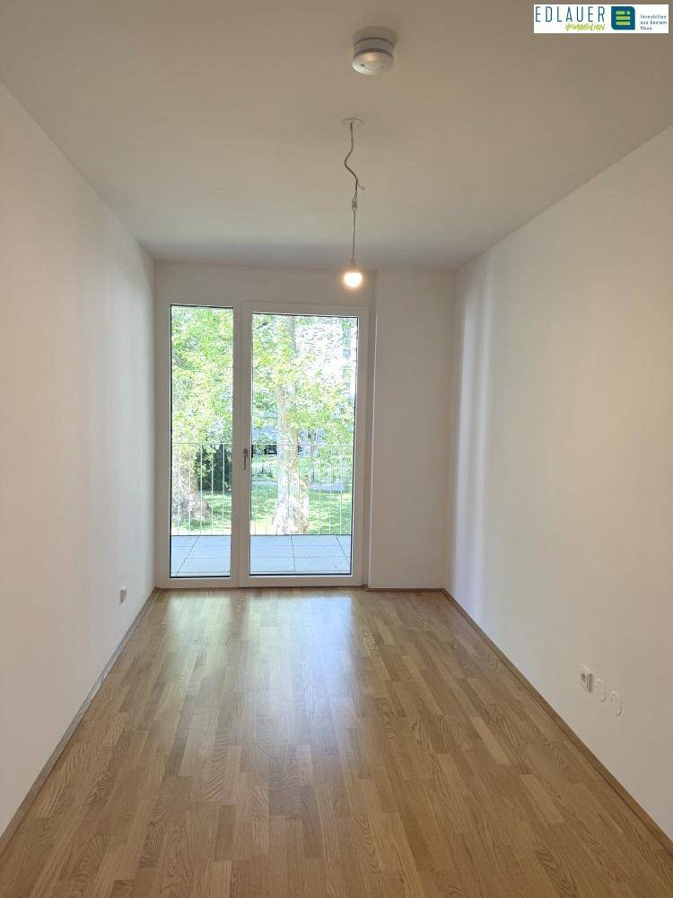 Heller, leerer Raum mit Holzparkettboden und großem Fenster mit Zugang zum Balkon.