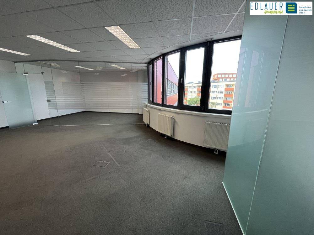 Moderner Büroraum mit geschwungenen Fenstern, Teppichboden und Glastrennwänden, bietet eine helle Arbeitsumgebung.