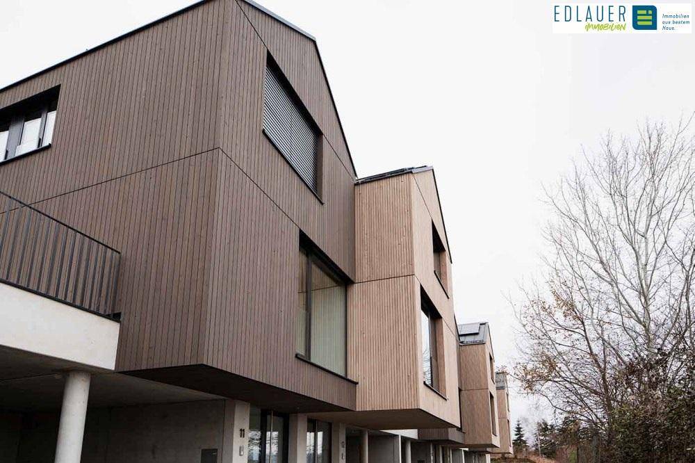 Seitenansicht der modernen Reihenhäuser mit Holzfassade und Balkonen, darunterliegenden Parkplätzen.