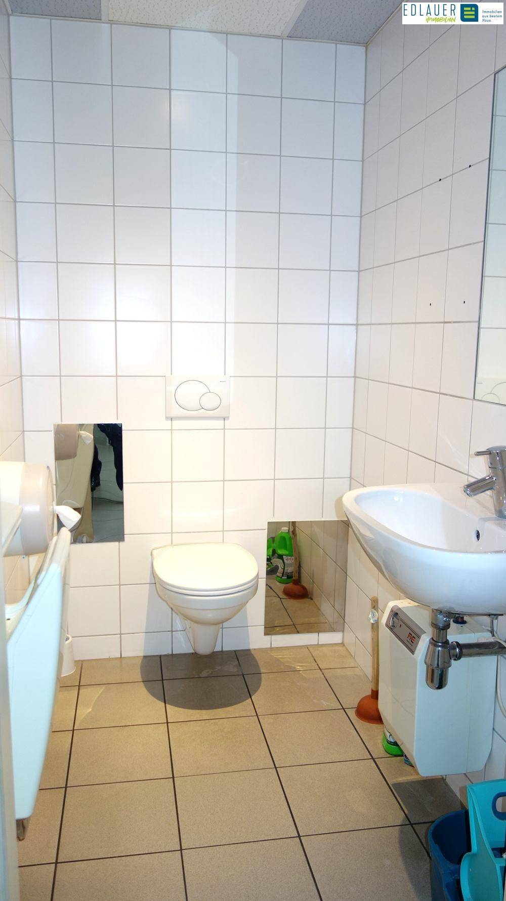 Badezimmer mit weißen Fliesen, einer wandmontierten Toilette und einem Waschbecken, das auf einem Unterschrank montiert ist.