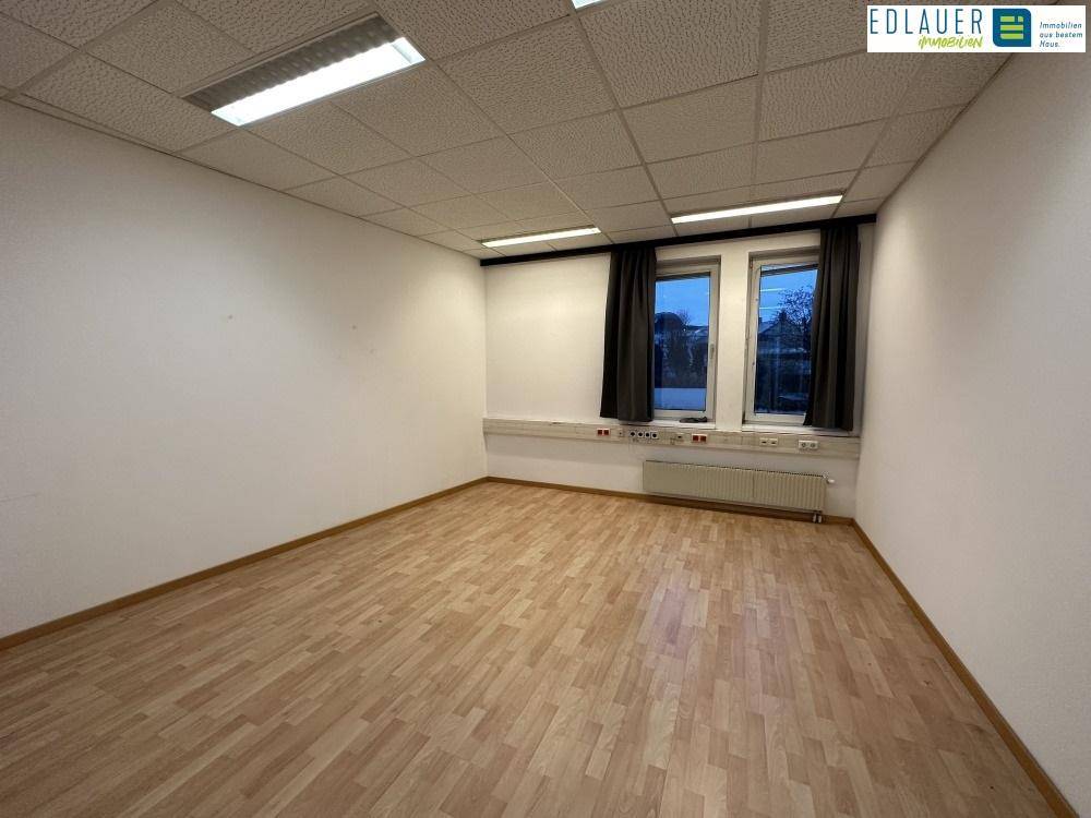 Leerer Büroraum mit Laminatboden, weißen Wänden und zwei Fenstern, ideal für flexible Nutzung.
