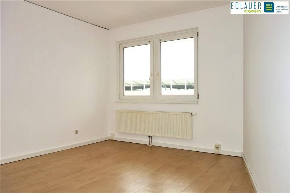 Unmöbliertes Zimmer mit Parkettboden, großen Fenstern und weiß gestrichenen Wänden.