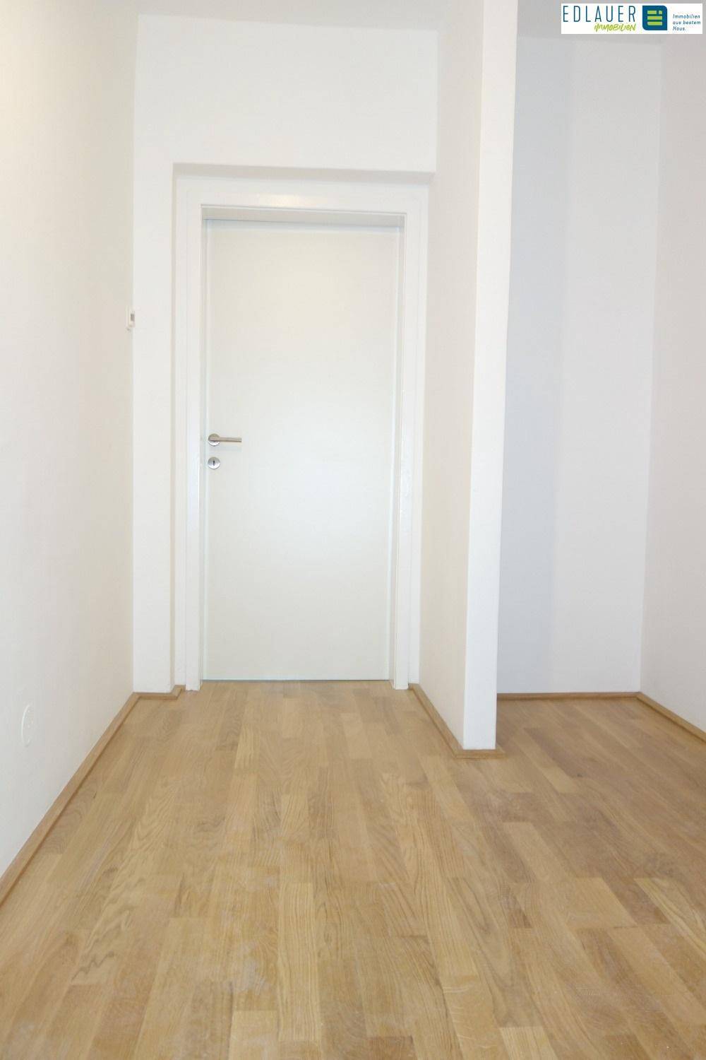 Heller Flur mit Parkettboden und weißer Tür, der zu weiteren Räumen führt.