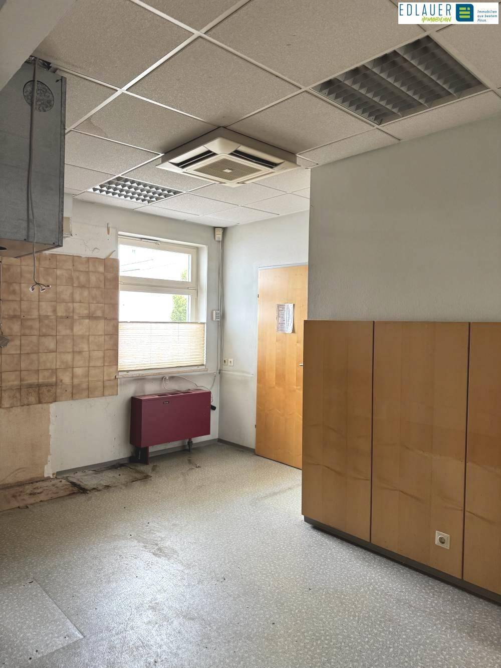 Raum mit Fliesenboden, einem Fenster und einer Heizung, der Renovierungsbedarf zeigt.