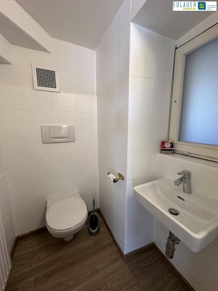 Kleines Badezimmer mit WC, Waschbecken, Fenster und weißen Wandfliesen, funktional und hell.