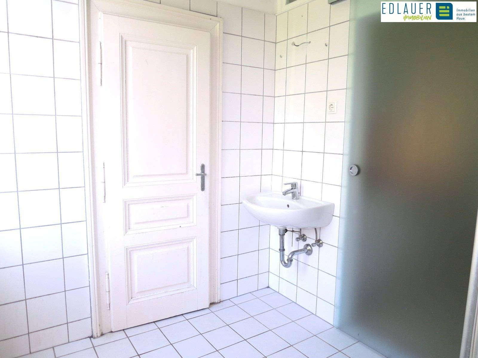 Gefliestes Badezimmer mit Waschbecken und einer Milchglastür, die Privatsphäre bietet.