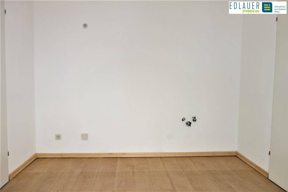 Leerer Raum mit Parkettboden und Anschlüssen an der Wand, möglicherweise für eine Küche.