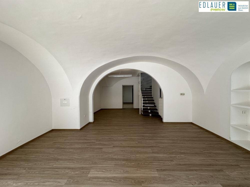 Weitläufiger Gewerberaum mit Gewölbedecken, Laminatboden und Blick auf die Fensterfront und den Treppenbereich.