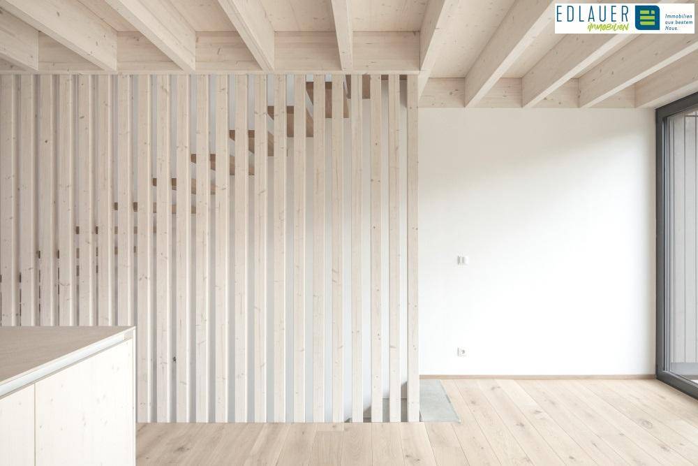 Offener Wohnbereich mit Holzbalkendecke, Holzlamellenwand und Blick auf eine Treppe.