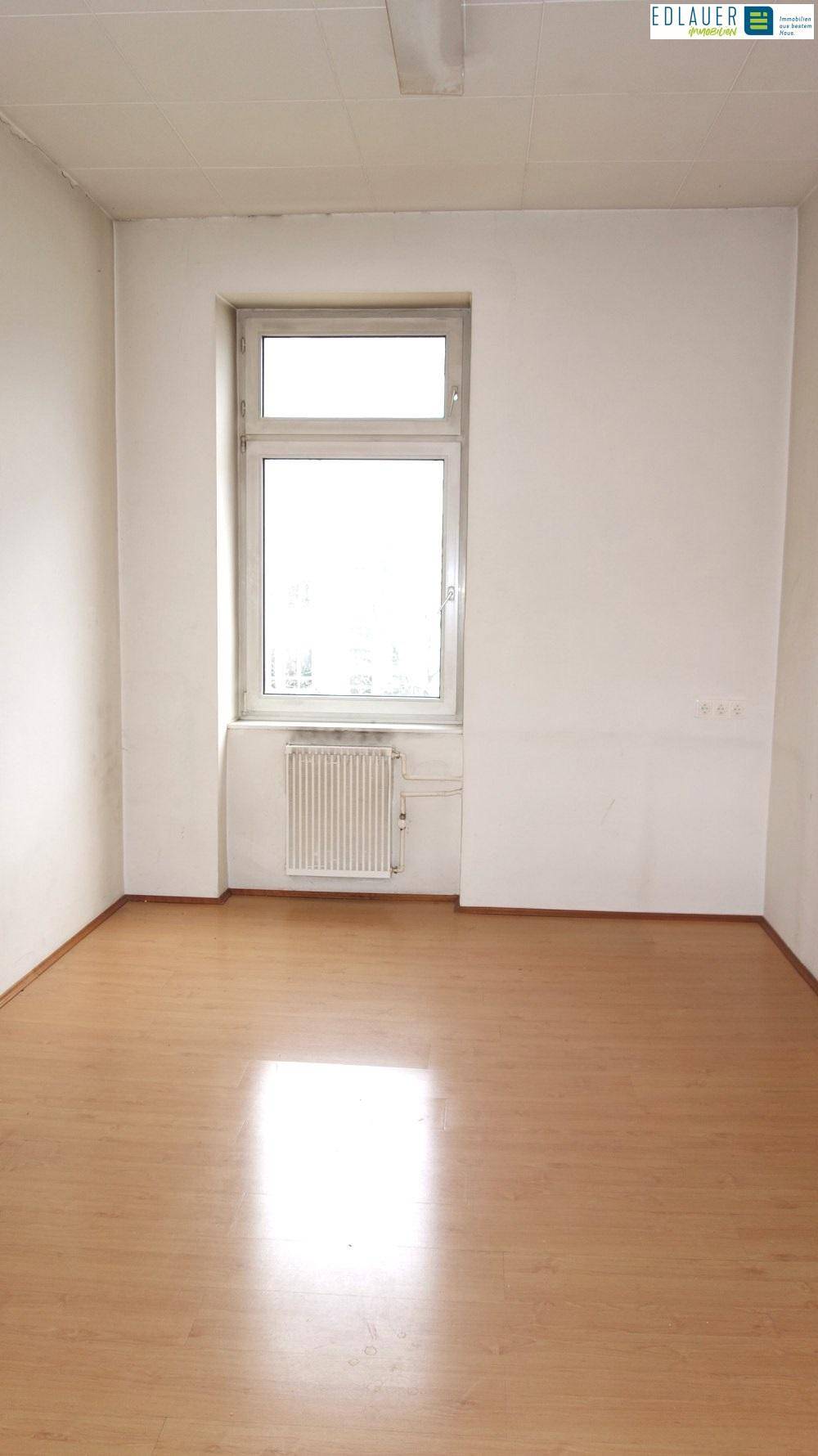 Heller Raum mit einem Fenster, Laminatboden und einem Heizkörper unter der Fensterbank.