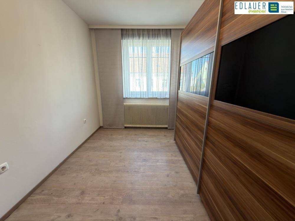 Schlafzimmer mit Laminatboden, großem Fenster und integriertem Kleiderschrank.