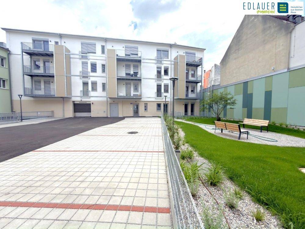 Gepflegter Gartenbereich mit Sitzbänken und Grünflächen hinter dem modernen Wohngebäude.