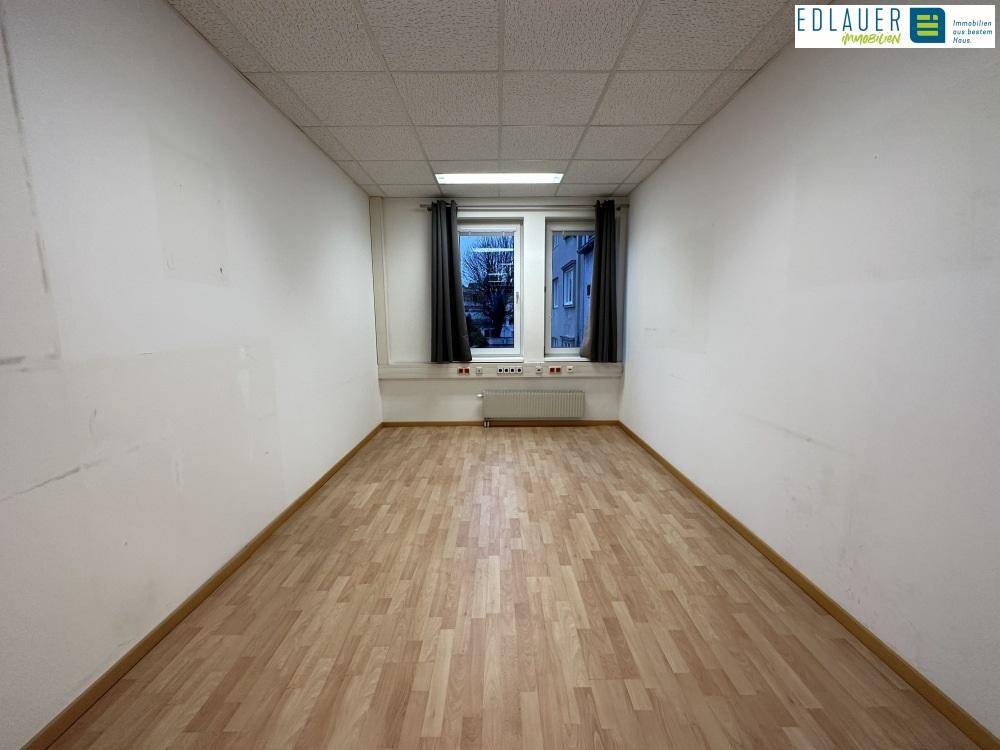 Schmalerer Büroraum mit Laminatboden und zwei Fenstern, bietet eine funktionale Arbeitsumgebung.