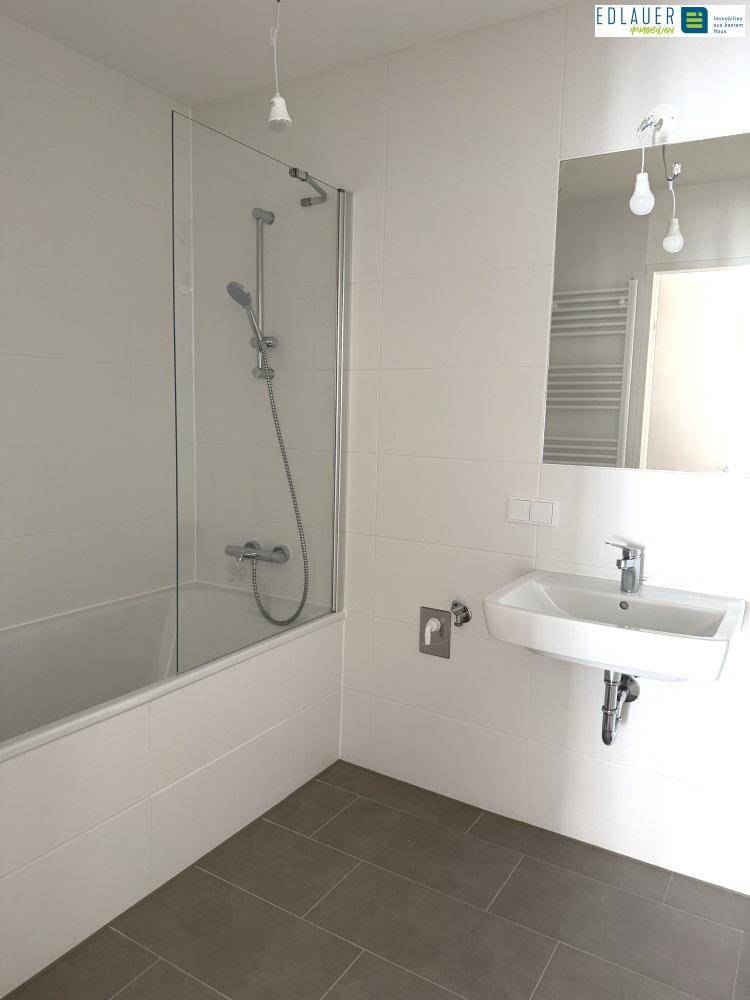 Helles Badezimmer mit Badewanne, Duschabtrennung, Waschbecken und großem Spiegel.