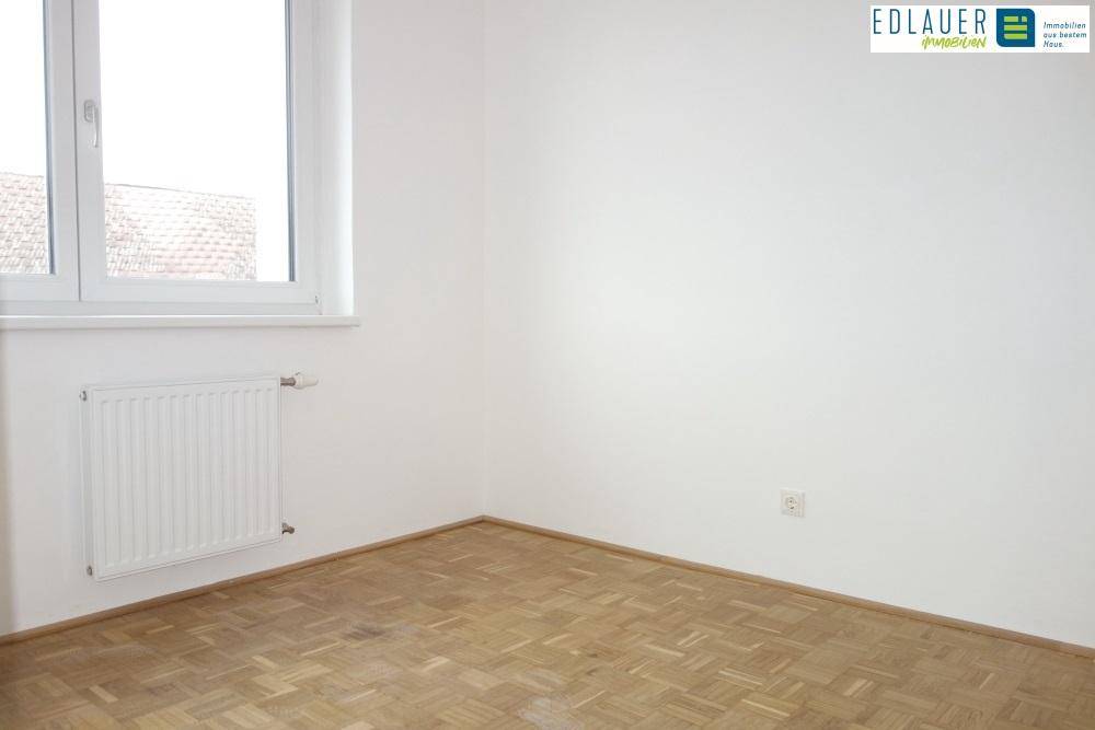 Heller, leerer Raum mit Parkettboden, weißen Wänden und einem Fenster.