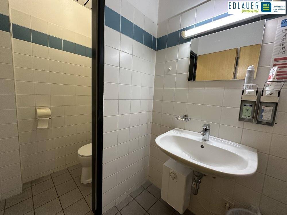 Sanitärraum mit Waschbecken, Toilette und weißen Fliesen, bietet grundlegende Ausstattung.