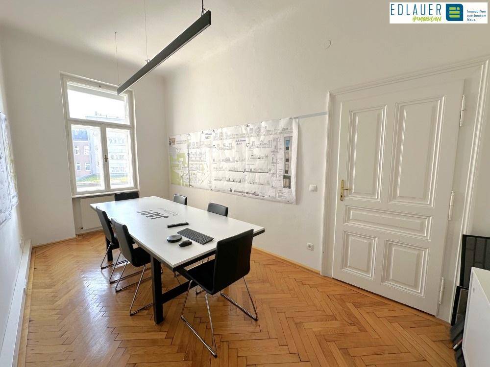 Besprechungsraum mit Holzboden, großem Tisch und natürlichem Lichteinfall durch ein hohes Fenster, perfekt für Team-Meetings.