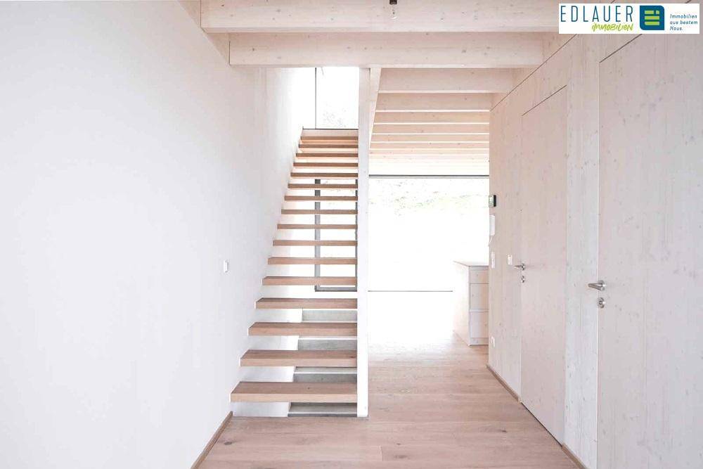 Heller Flur mit moderner Holztreppe und hellen Holzverkleidungen an Wänden und Decke.