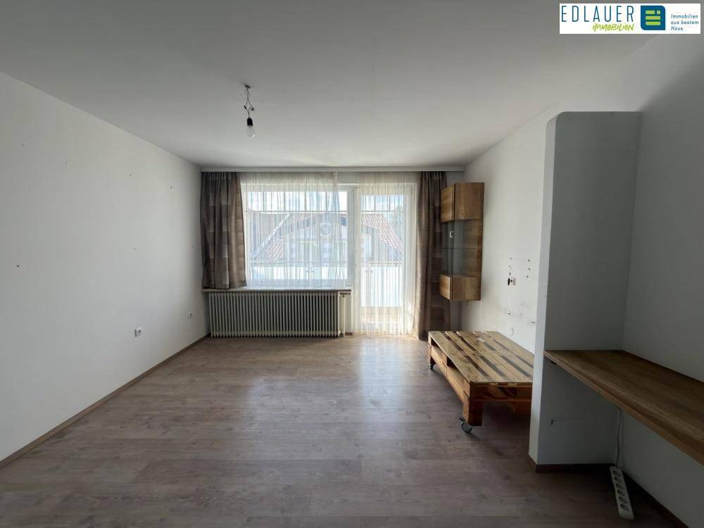 Geräumiges Wohnzimmer mit Laminatboden, großem Fenster und Heizkörper unter dem Fenster.
