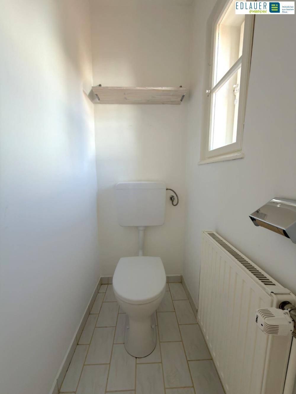 Separates WC mit Fenster, Toilette und Fliesenboden, hell und funktional.