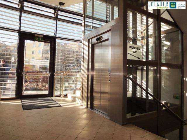 Heller Eingangsbereich mit Glasfassade, Aufzug und Treppe, bietet Zugang zu den oberen Etagen.