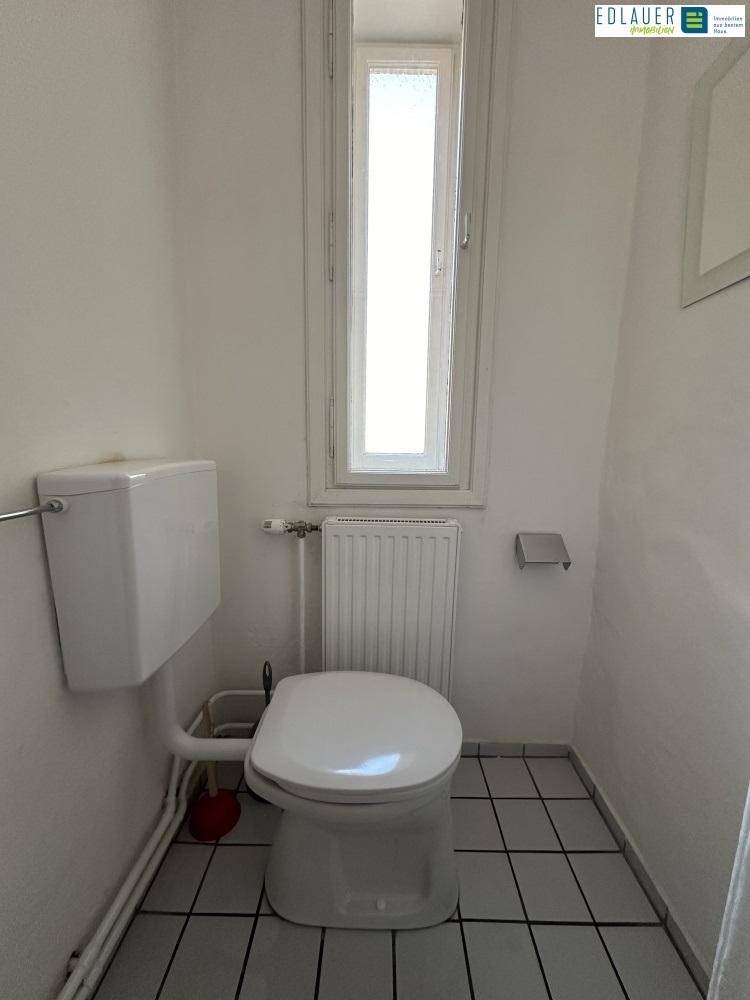 Kleiner Toilettenraum mit WC, hohem schmalen Fenster und Fliesenboden, funktional und hell.