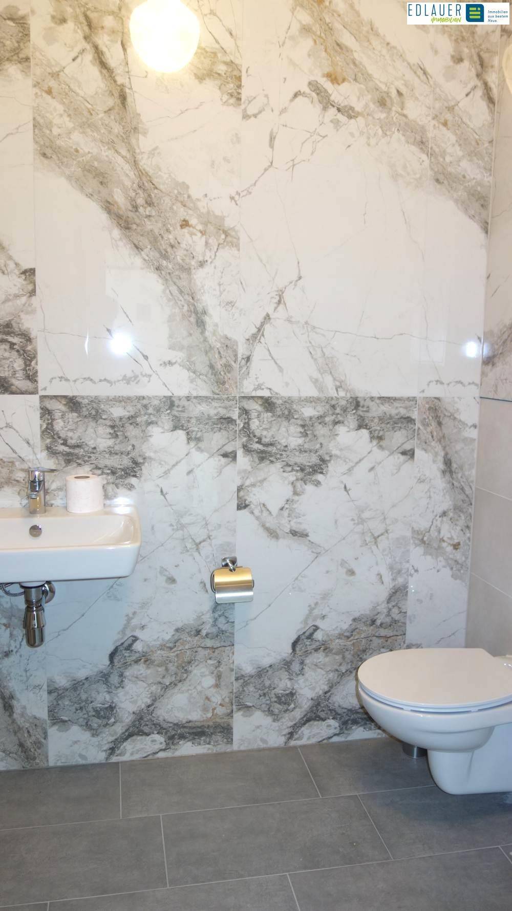 Badezimmer mit Wand-WC, Waschbecken und eleganten Marmor-Effekt-Fliesen.