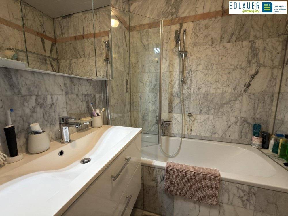 Badezimmer mit Marmorfliesen, Badewanne und modernem Waschtisch mit Spiegel.