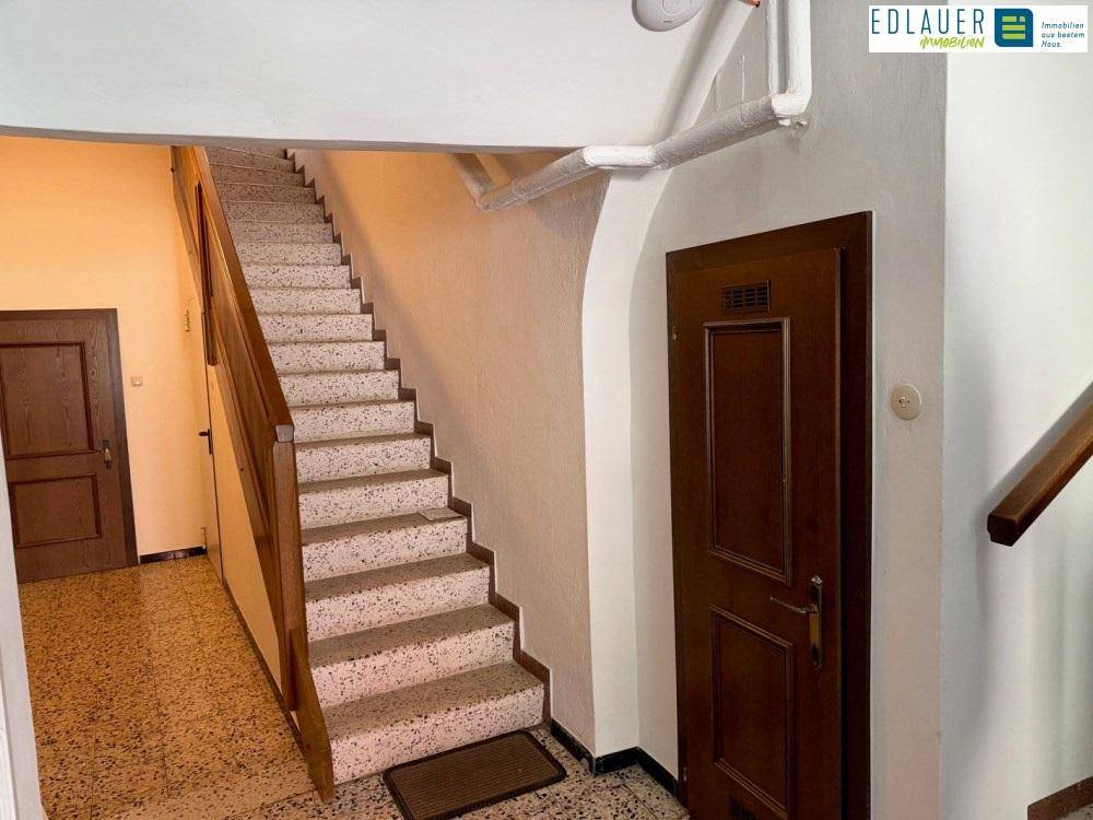 Heller Treppenaufgang mit Terrazzostufen und Holzgeländer in einem Mehrfamilienhaus.