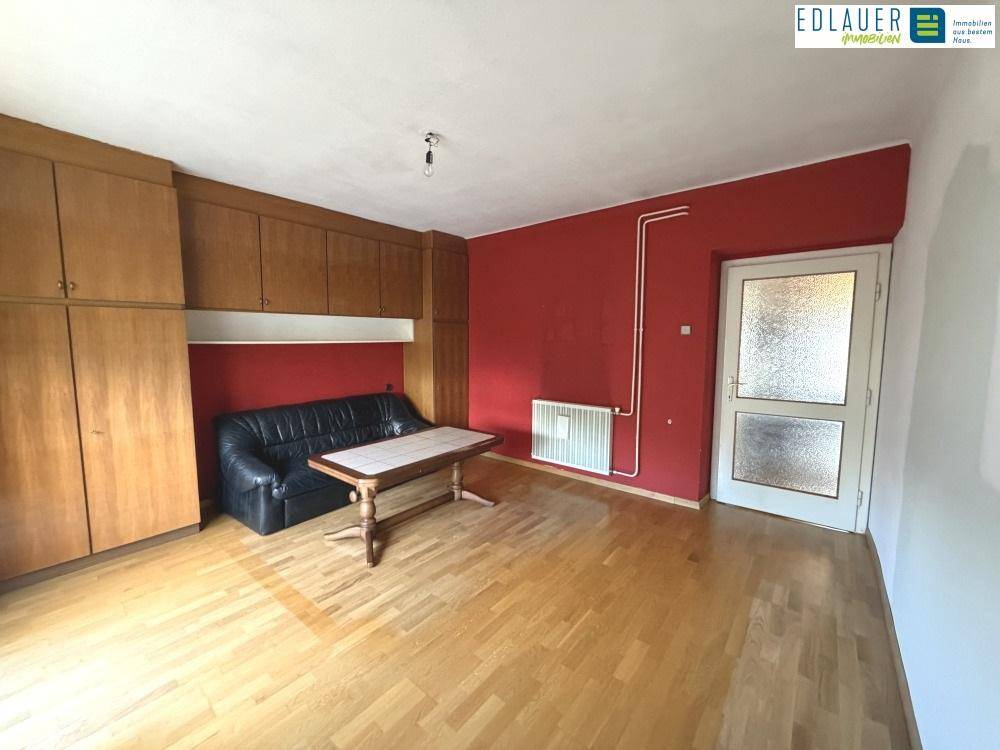 Wohnzimmer mit roter Akzentwand, Parkettboden und Heizkörper, bereit zur individuellen Gestaltung.