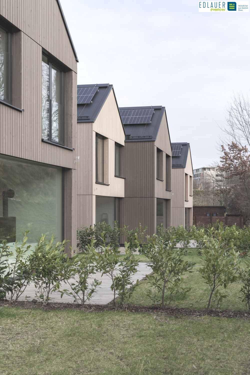 Gepflegte Gärten hinter den modernen Reihenhäusern mit Holzfassaden und großen Fenstern.