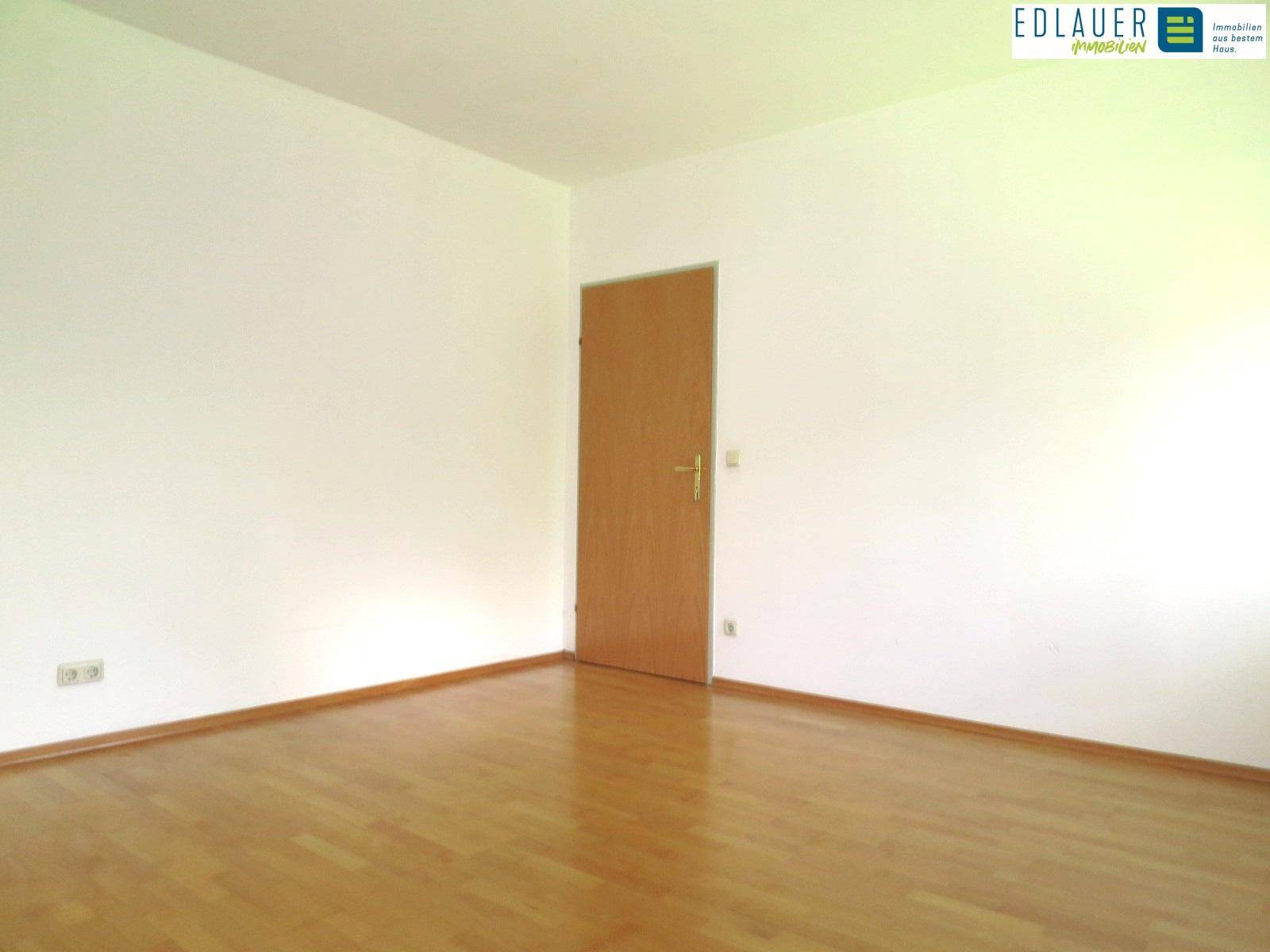 Heller Raum mit Holztür und Parkettboden, bereit zur individuellen Gestaltung.