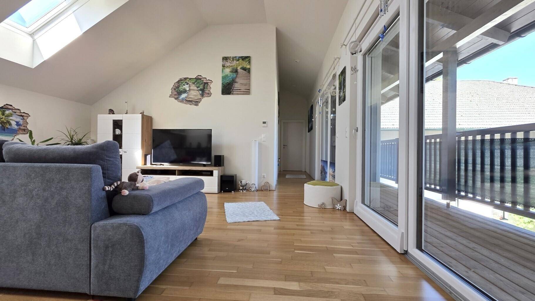 Heller Wohnbereich mit Holzboden, Dachfenstern und Zugang zu einem langen Balkon.