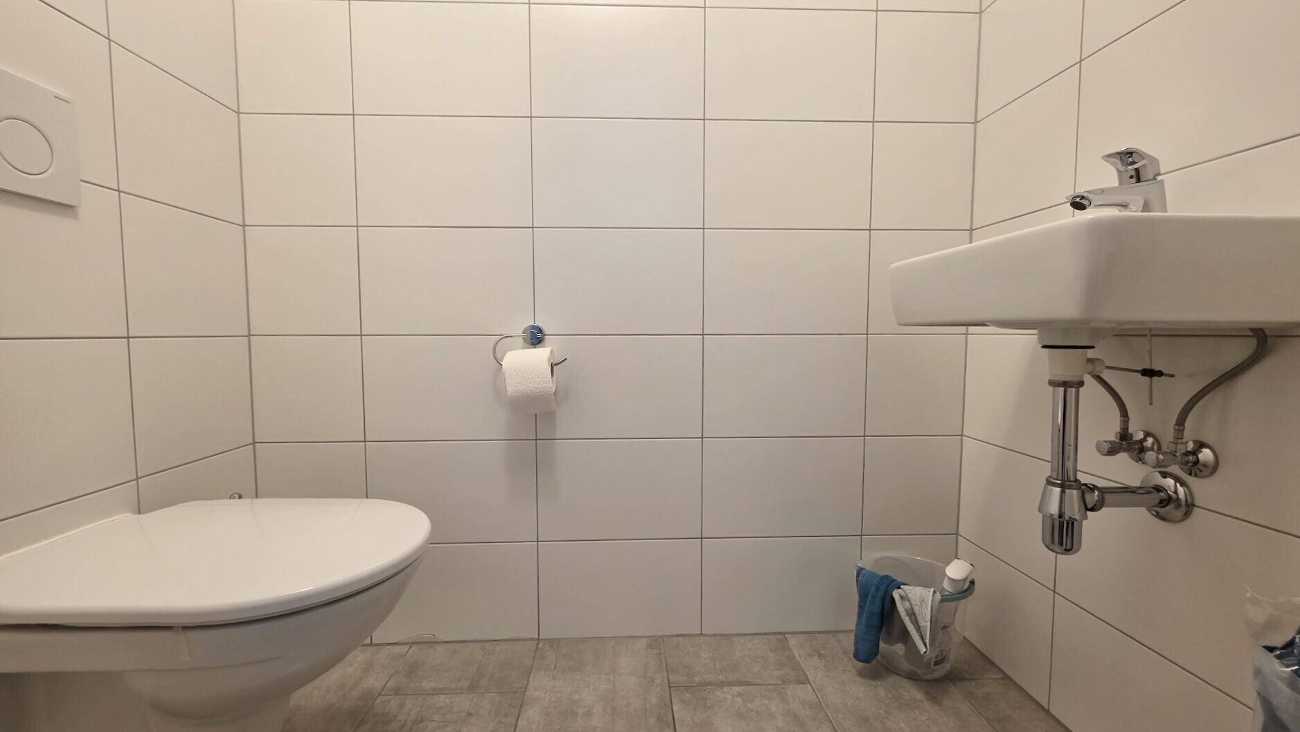Kleines WC mit weißen Fliesen, wandmontierter Toilette und Waschbecken.