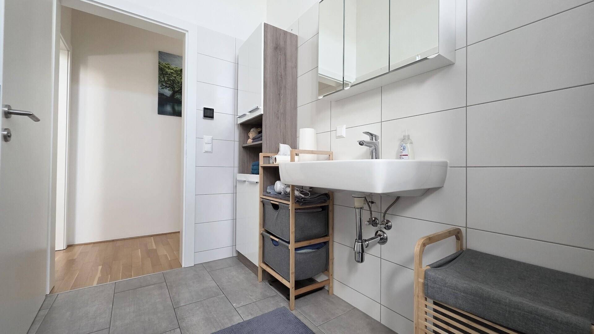 Modernes Badezimmer mit weiß gefliesten Wänden, Waschbecken und Spiegelschrank.