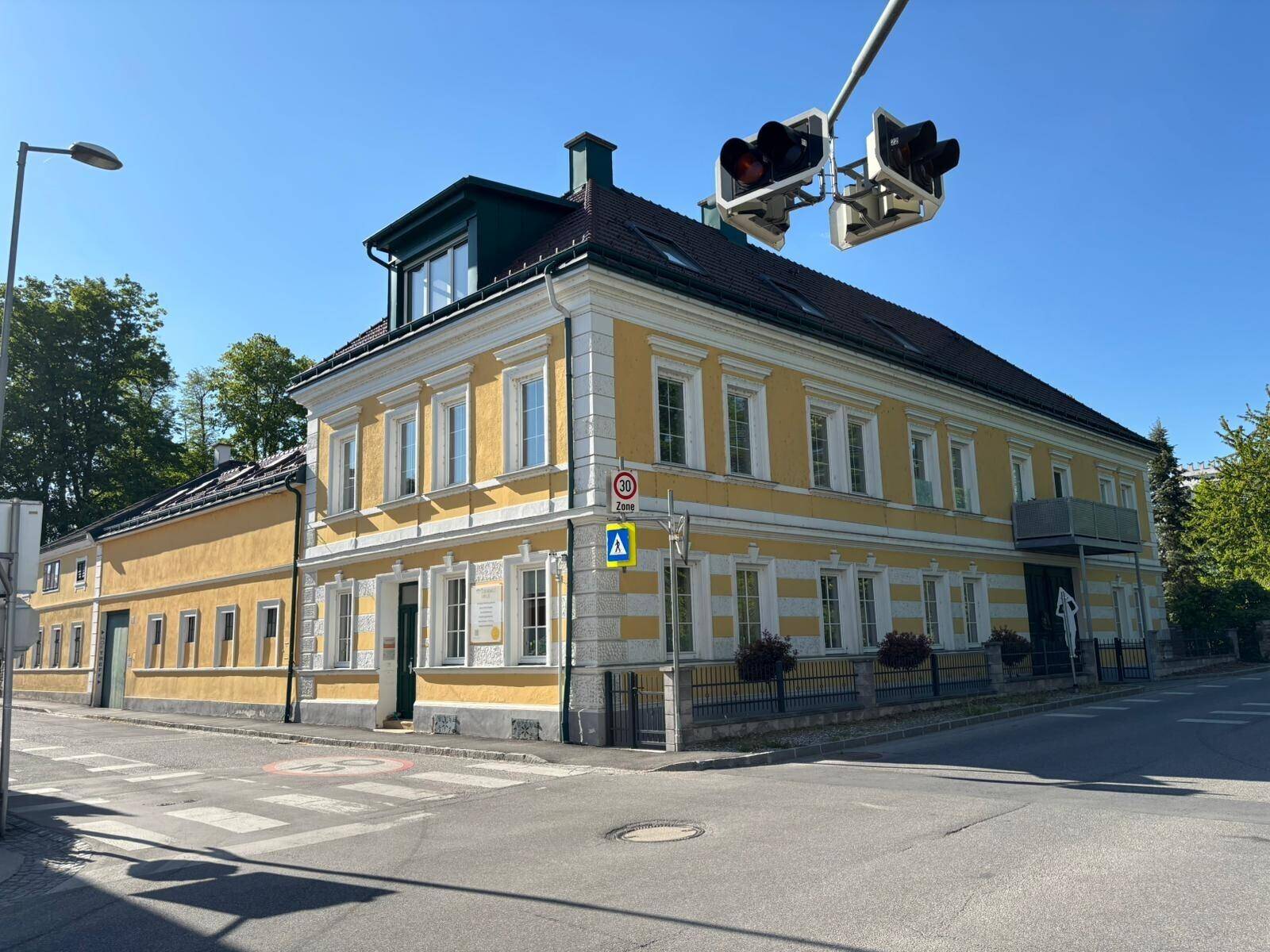 Historisches Gebäude mit gelber Fassade an einer Straßenecke unter blauem Himmel.