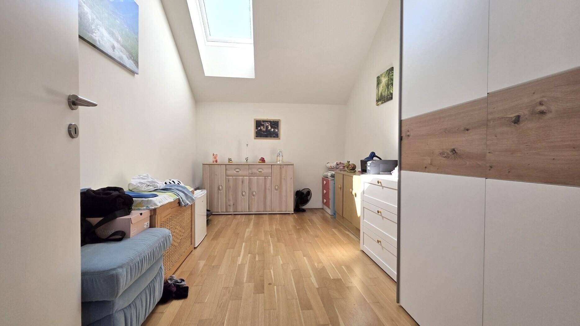 Schlafzimmer mit Dachschräge, Holzboden und einem Dachfenster für natürliches Licht.